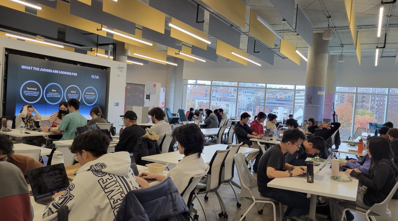 Students working at tables during a NOVA event, with a screen that reads What the judges are looking for.