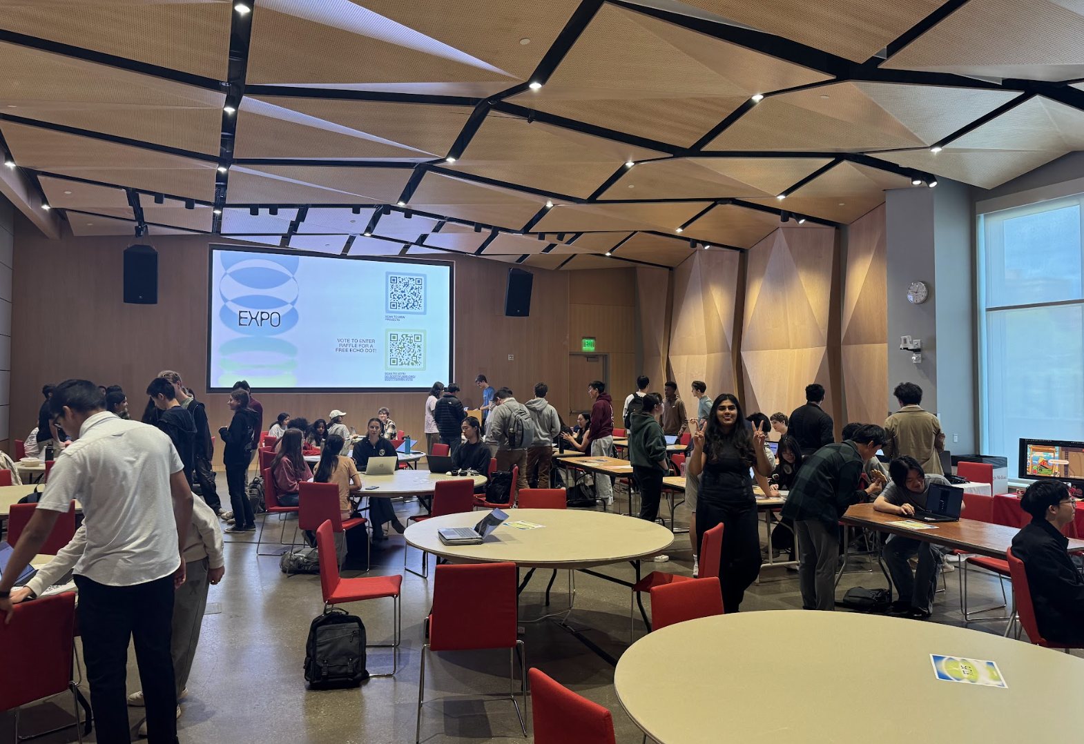 A crowded expo hall with round tables and a screen that reads EXPO, from ScottySpark.